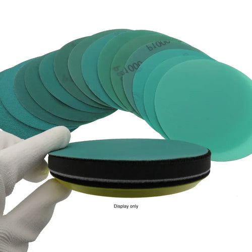 Teal sanding disc with hook-and-loop backing ring, shown held by a gloved hand