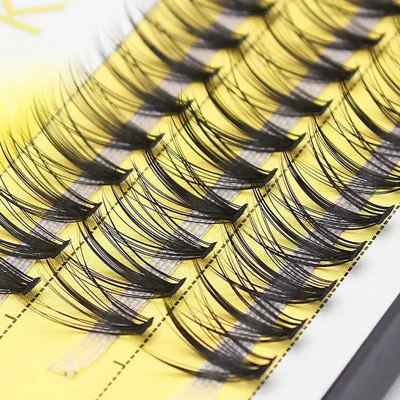 A tray of black 20D Russian volume eyelash clusters, arranged on a yellow strip for professional application.