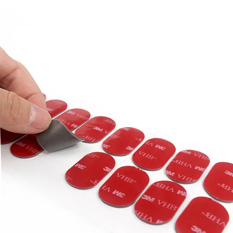 Hand placing a round die-cut double-sided acrylic foam tape pad with red adhesive