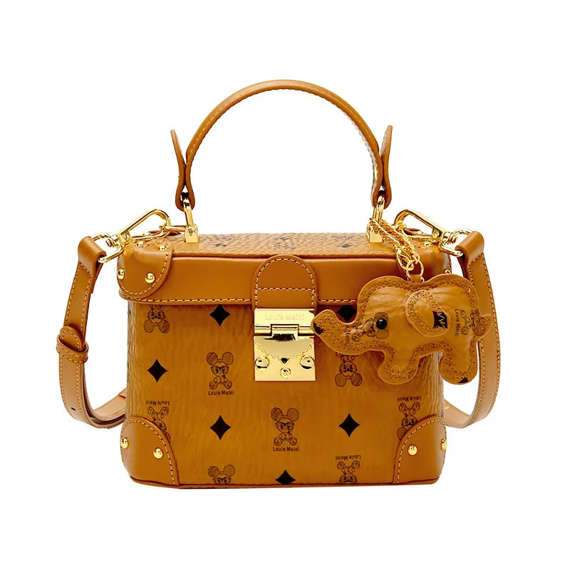 Tan cowhide trunk handbag with gold hardware, monogram print, and playful elephant charm for women.