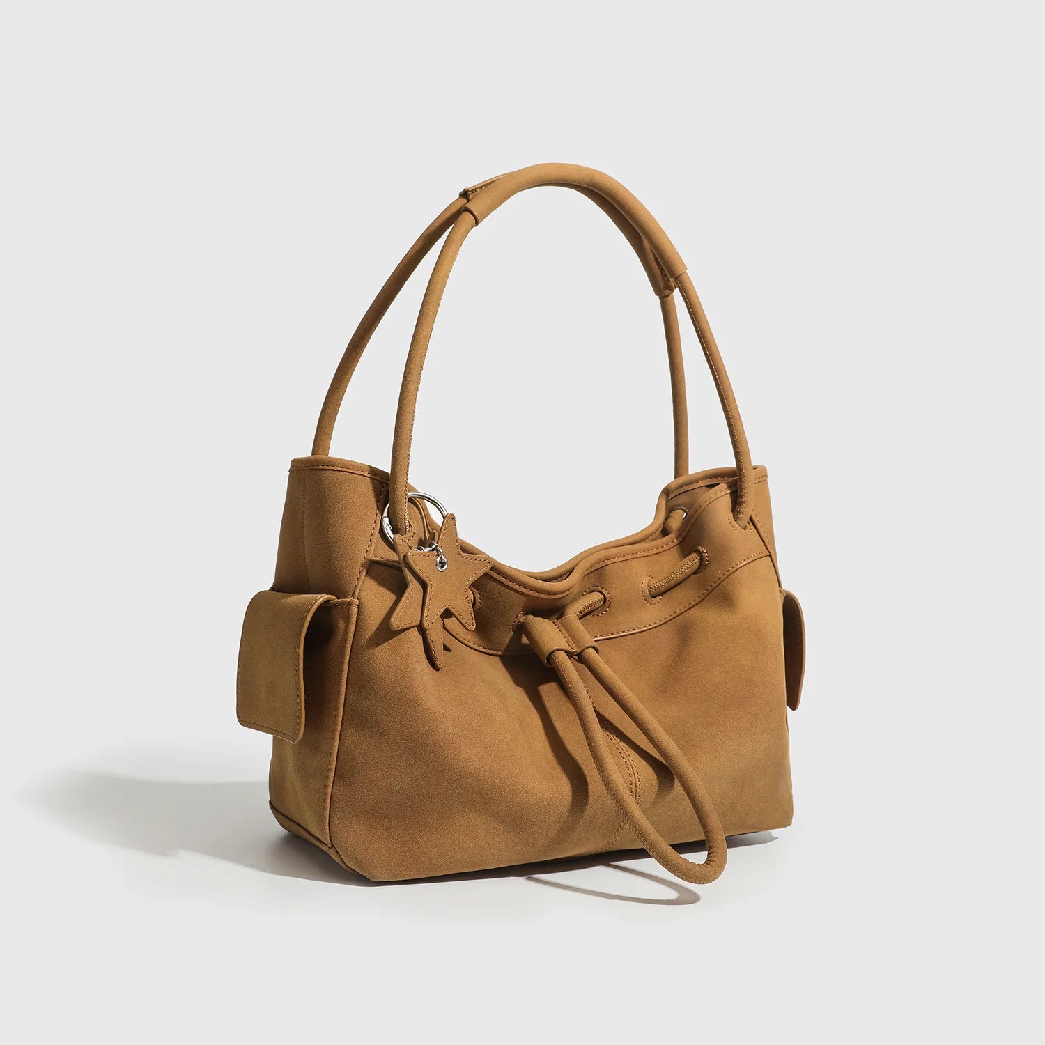 Tan suede underarm shoulder bag with drawstring, star charm, and dual straps. Stylish large capacity commuting tote.