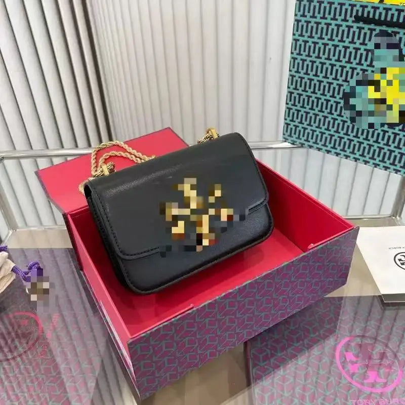 Black leather Zhenwo TB trunk crossbody bag with gold metal hardware, chain strap, and front logo in a branded box.