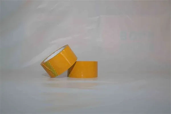 Yellow packing tape rolls stacked, pressure-sensitive acrylic adhesive, green dot backing