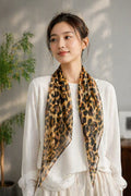 Luxury silk scarf with brown and black leopard print, triangular shape, worn around neck by a woman in a white top.