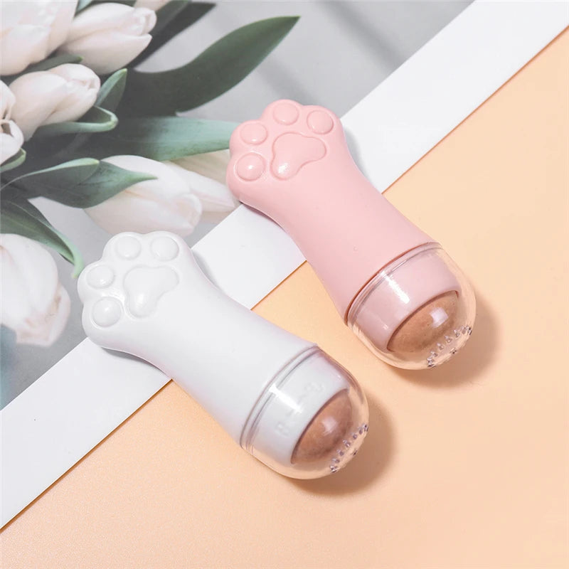 Two cat-paw-shaped volcanic stone facial oil rollers in white and pink, positioned on a floral-themed background.