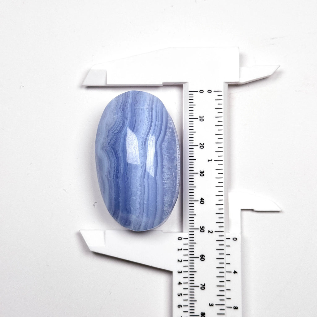 Blue lace agate palm stone beside a ruler, smooth oval gemstone with blue and white stripes