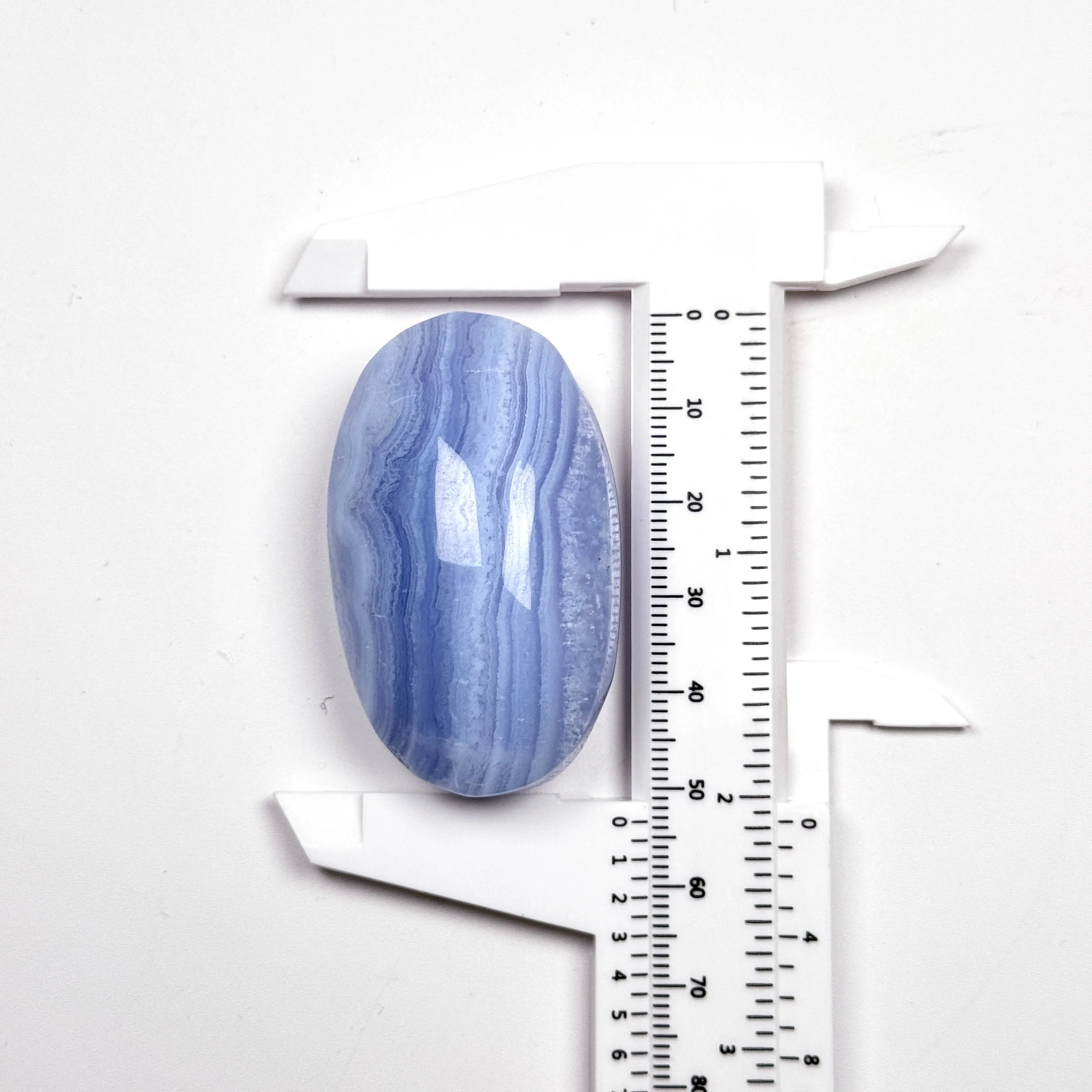 Blue lace agate palm stone beside a ruler, smooth oval gemstone with blue and white stripes