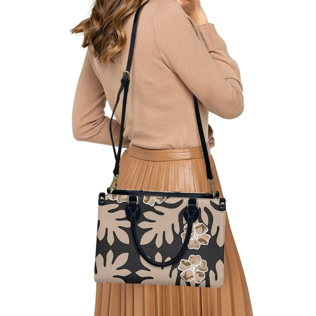 Tan and black leather handbag with Polynesian tribal floral pattern, shoulder strap, and top handles for women.