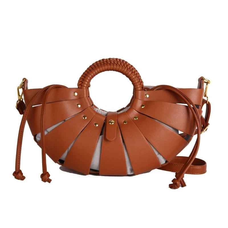 Brown half-moon trunk handbag with hollow-out leather straps, round braided handle, and drawstring fabric interior.
