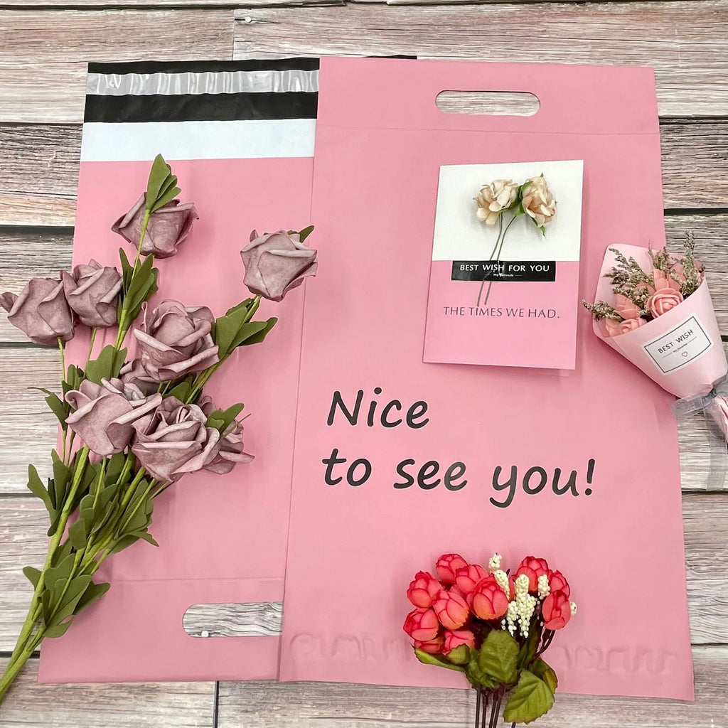 Pink poly mailer with handle cutout and small floral stickers, text on front
