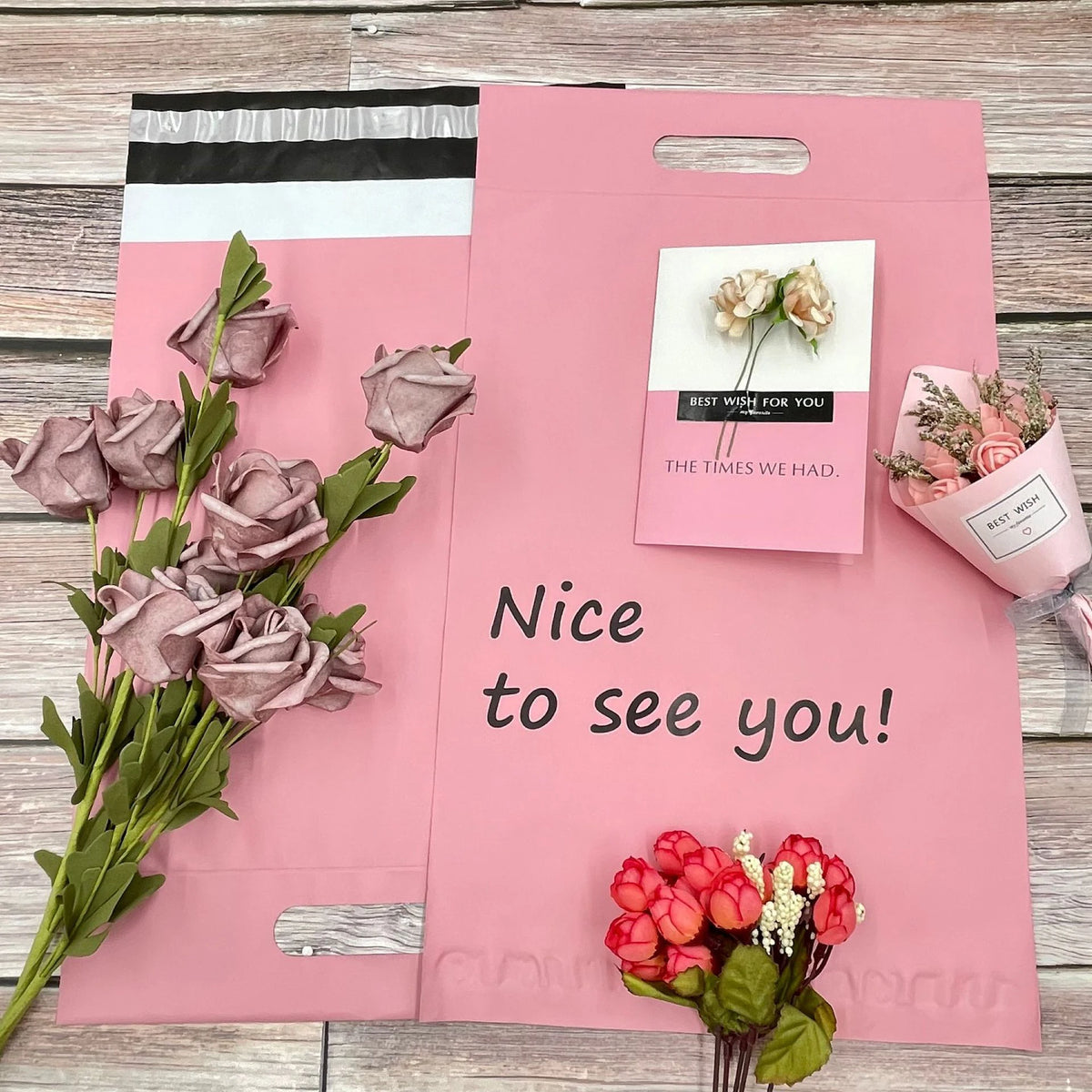 Pink poly mailer with handle cutout and small floral stickers, text on front