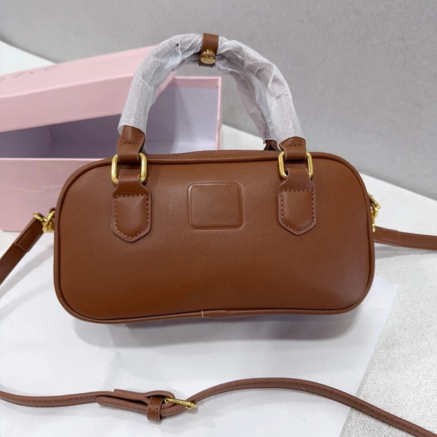 Small brown leather trunk handbag with gold hardware, dual top handles, and adjustable crossbody strap.