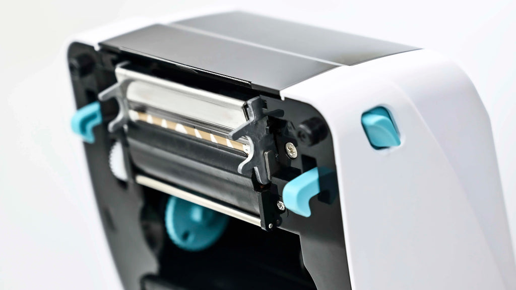 Direct thermal printer close-up of print head and ribbon mechanism in white housing.