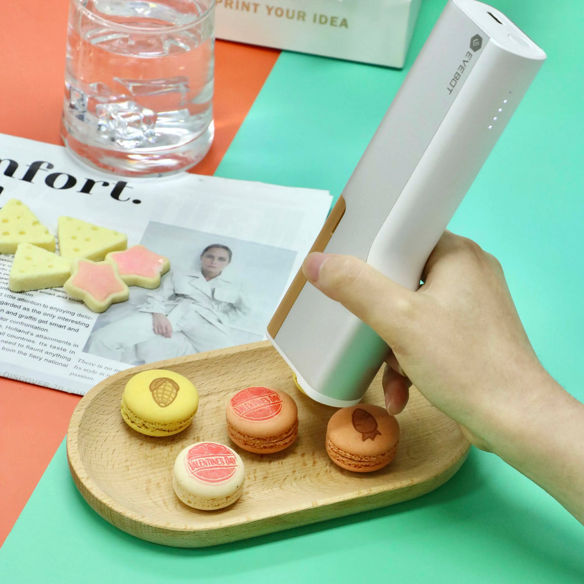 Handheld edible inkjet printer printing on macarons on a wooden tray with images.
