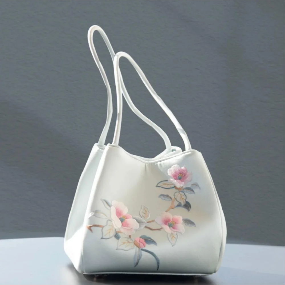 Pale blue silk shoulder bag featuring traditional Chinese floral Su embroidery and thin, elegant carrying straps.