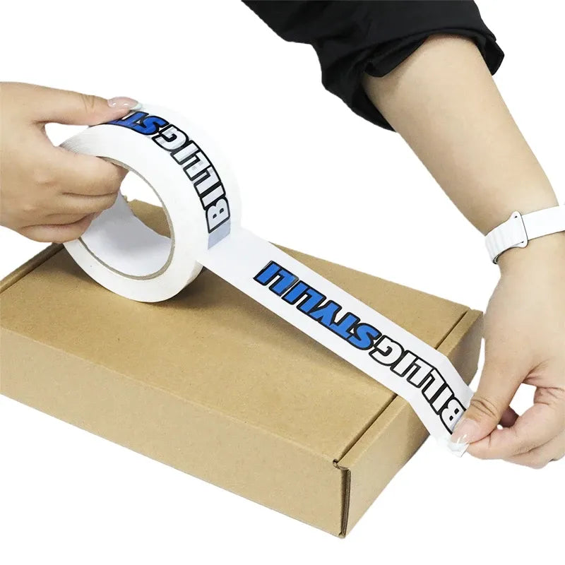 Hands applying printed packing tape to a cardboard box for parcel sealing