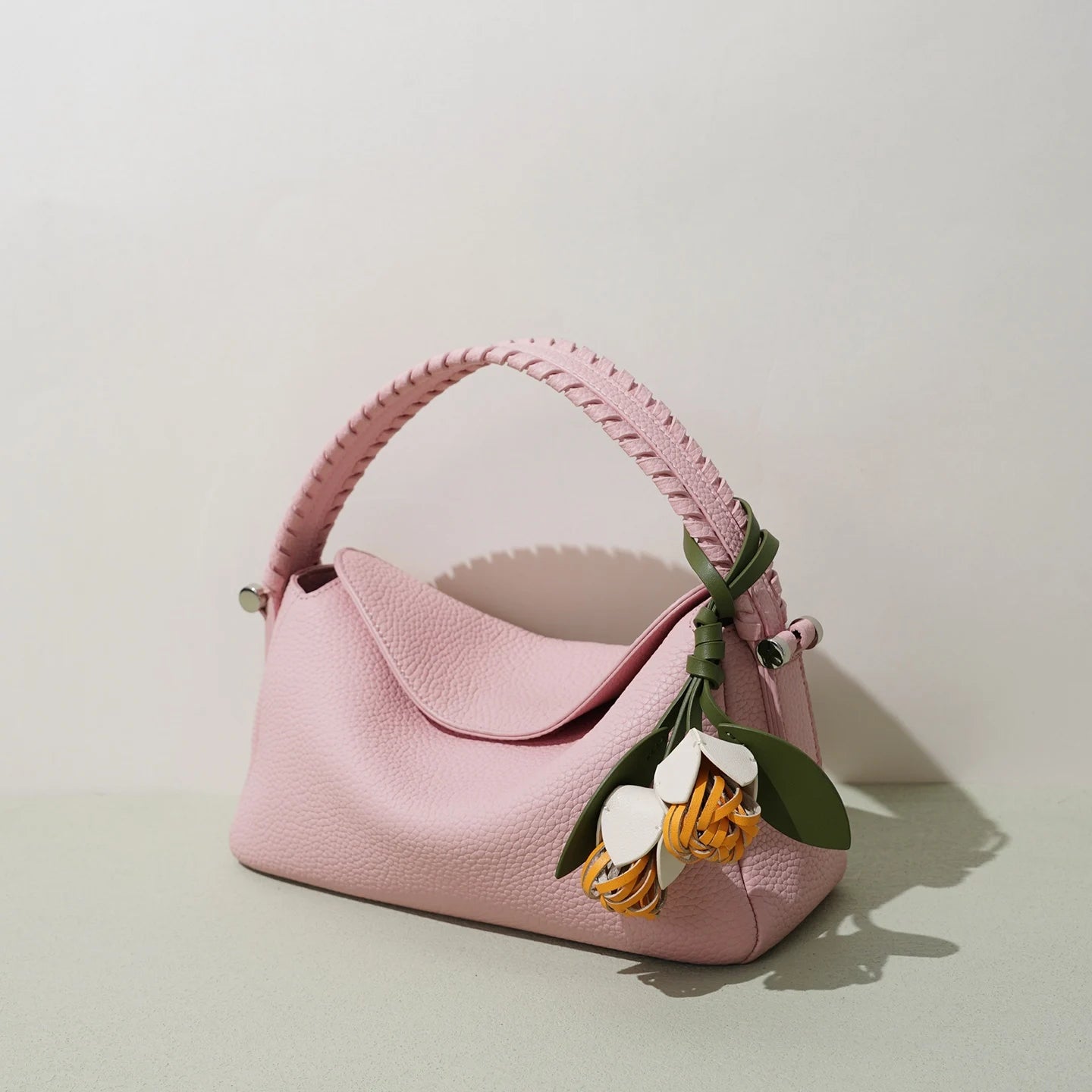 Pink genuine leather small tote with woven handle and detachable floral charm for women. Designer style crossbody bag.