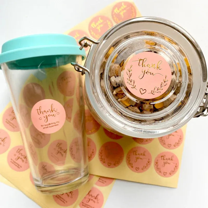 Pink round thank you stickers on packaged items and a clear jar