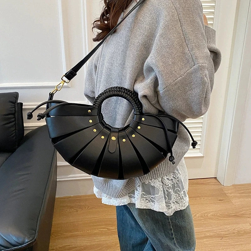 Black half-moon hollow-out trunk handbag with gold studs, round braided handle, and detachable shoulder strap.