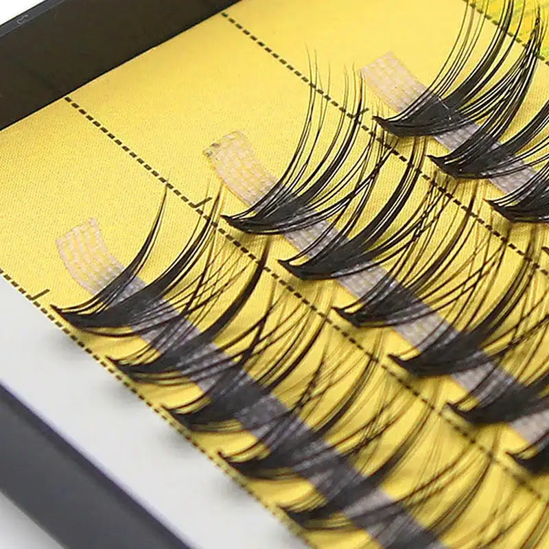 A tray of black 20D Russian volume eyelash clusters on a yellow background, arranged in rows.