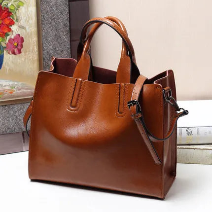 Tan genuine leather tote handbag with double handles, adjustable shoulder strap, and classic structured trunk design.