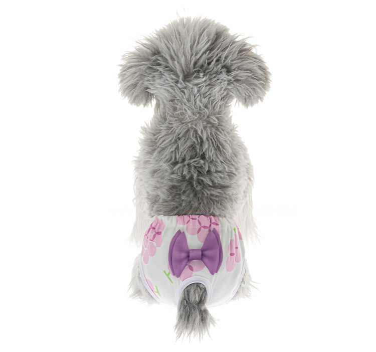 Small dog wearing washable, reusable floral sanitary diaper panties with a purple bow for female pet menstruation.