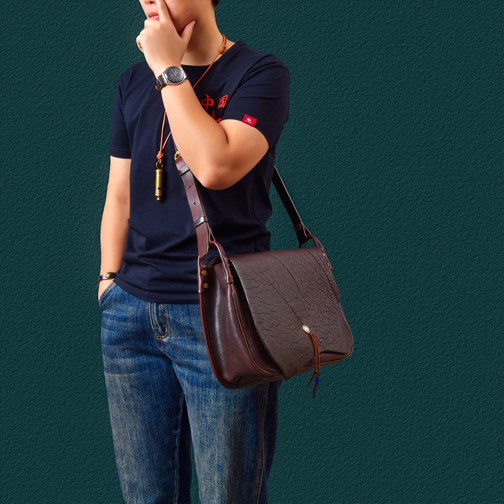 Vintage handmade dark brown cowhide messenger bag with a textured flap, brass button closure, and adjustable strap.