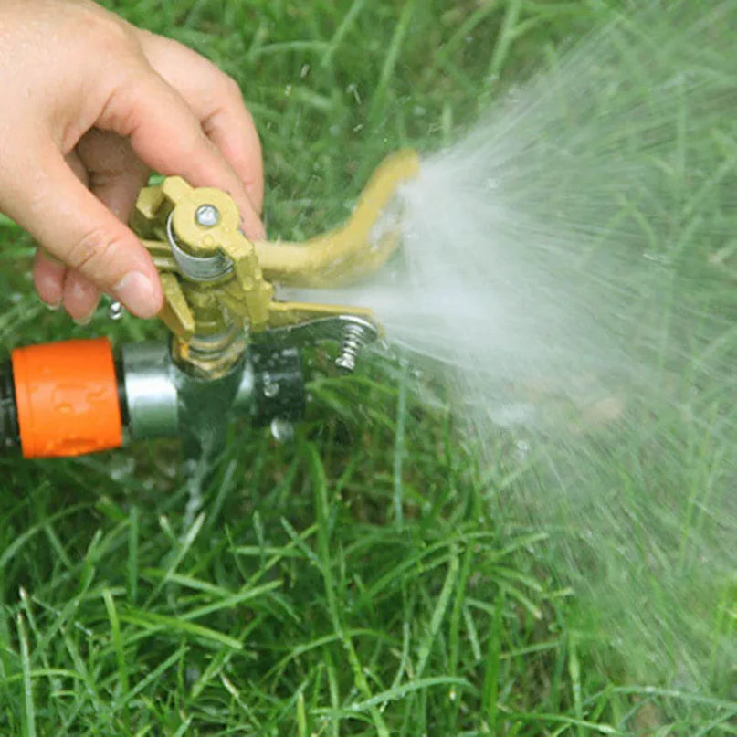 Gold rotating garden sprinkler spraying water from a hose connector over grass