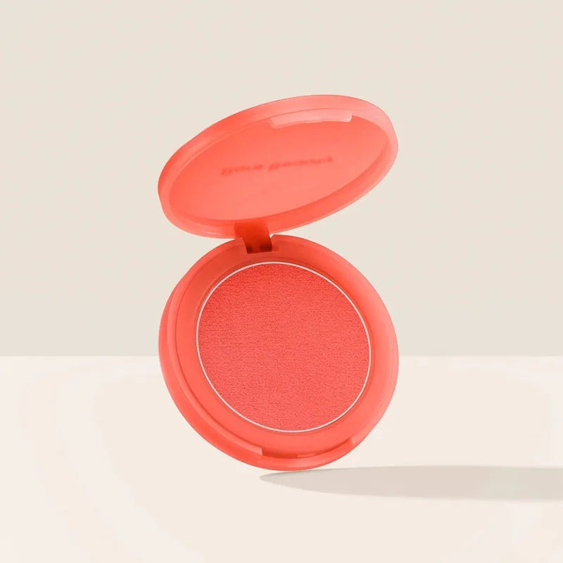 Rare Beauty soft matte powder blush in coral pink with a smooth, velvety texture in an open round compact.