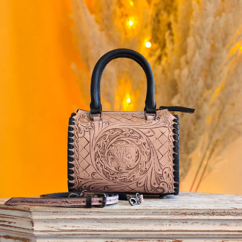 Luxury hand-tooled leather trunk bag with floral carving and playing card motif, black handles and stitched trim.