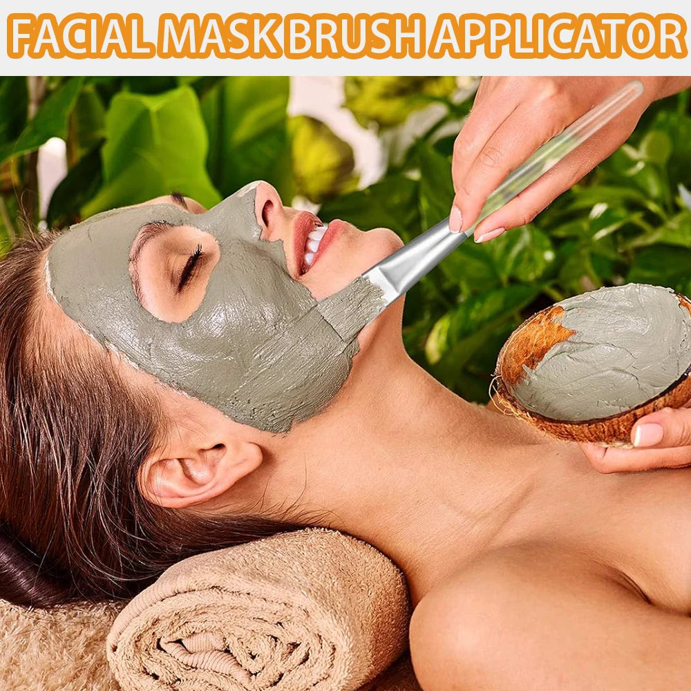 A woman applying gray clay mask to her face with a flat, transparent-handled brush from a coconut shell bowl.