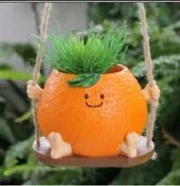 Mini hanging succulent planter, orange character face with small green plant on swing ropes.