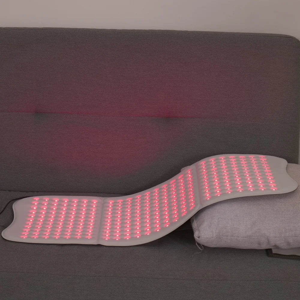 Large, flexible white light therapy mat with glowing red LED panels, resting on a gray sofa.