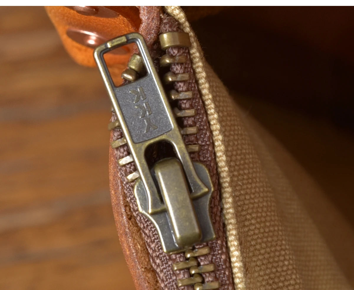 Close-up of PNDME vintage genuine cowhide leather messenger bag, featuring a durable brass YKK zipper and tan lining.