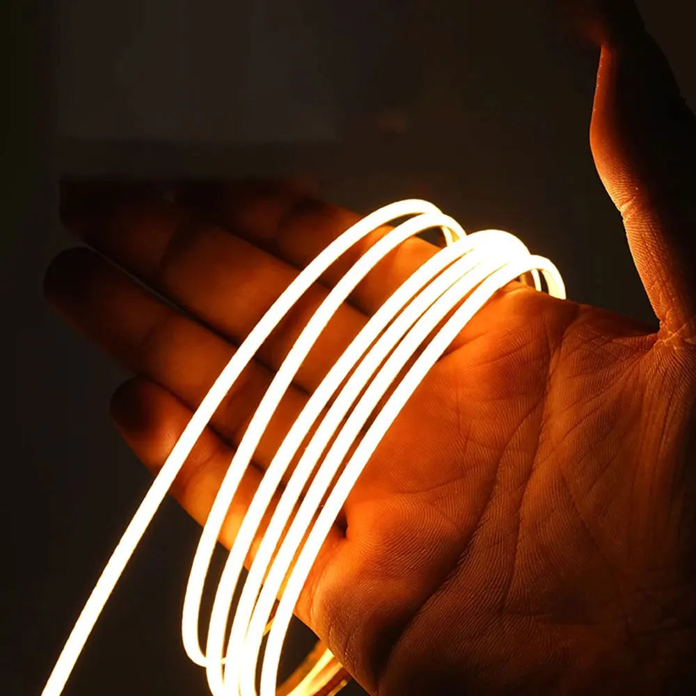 Flexible COB LED strip held in fingers, glowing warm white LEDs in tight coils