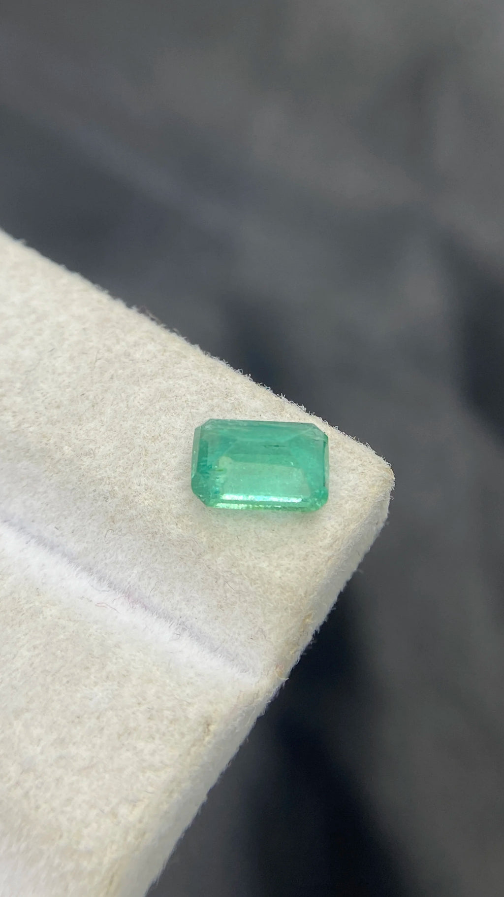 Loose emerald-cut green gemstone on white cushion, angled view.