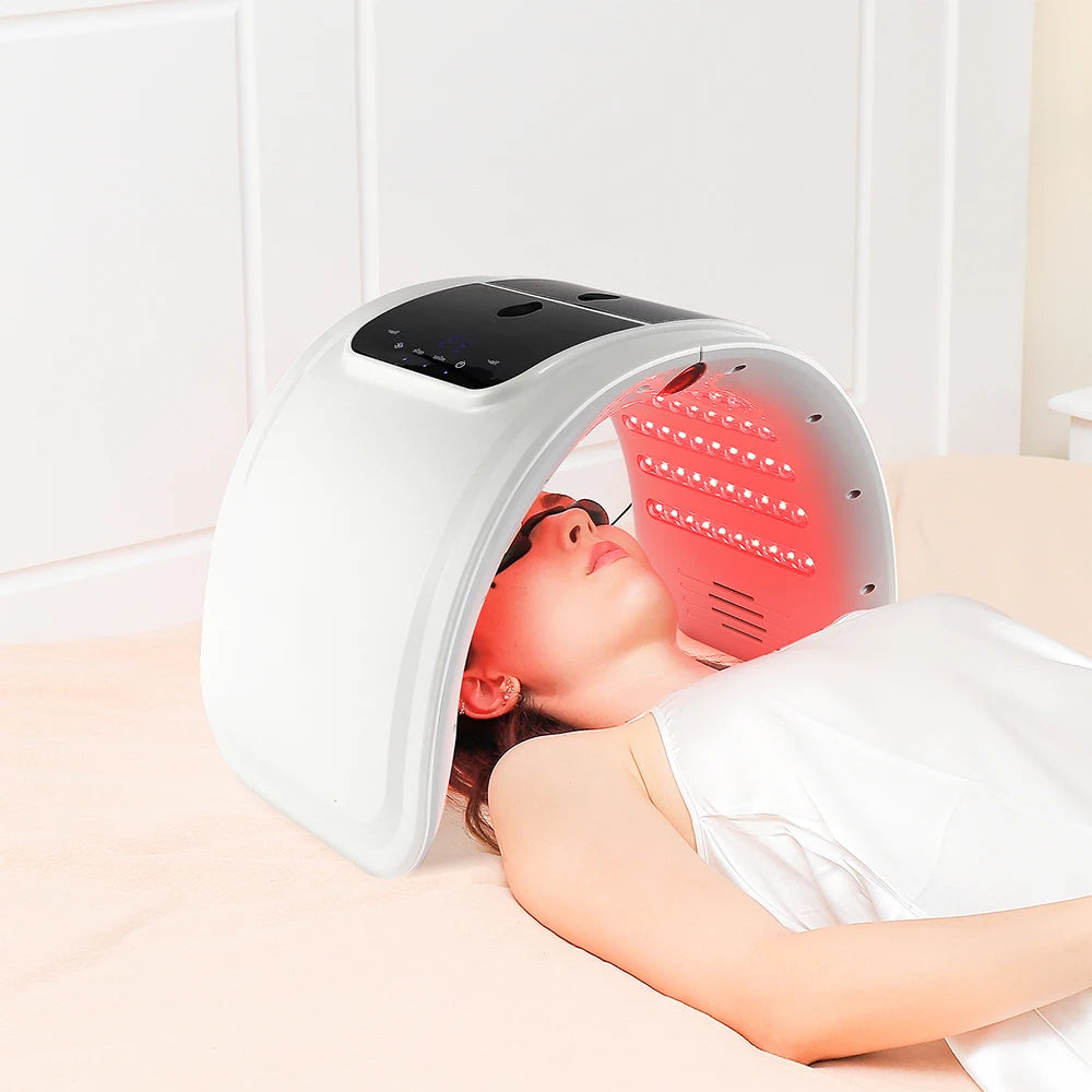 White arched LED light therapy machine over a person's face, emitting red light for skin rejuvenation.
