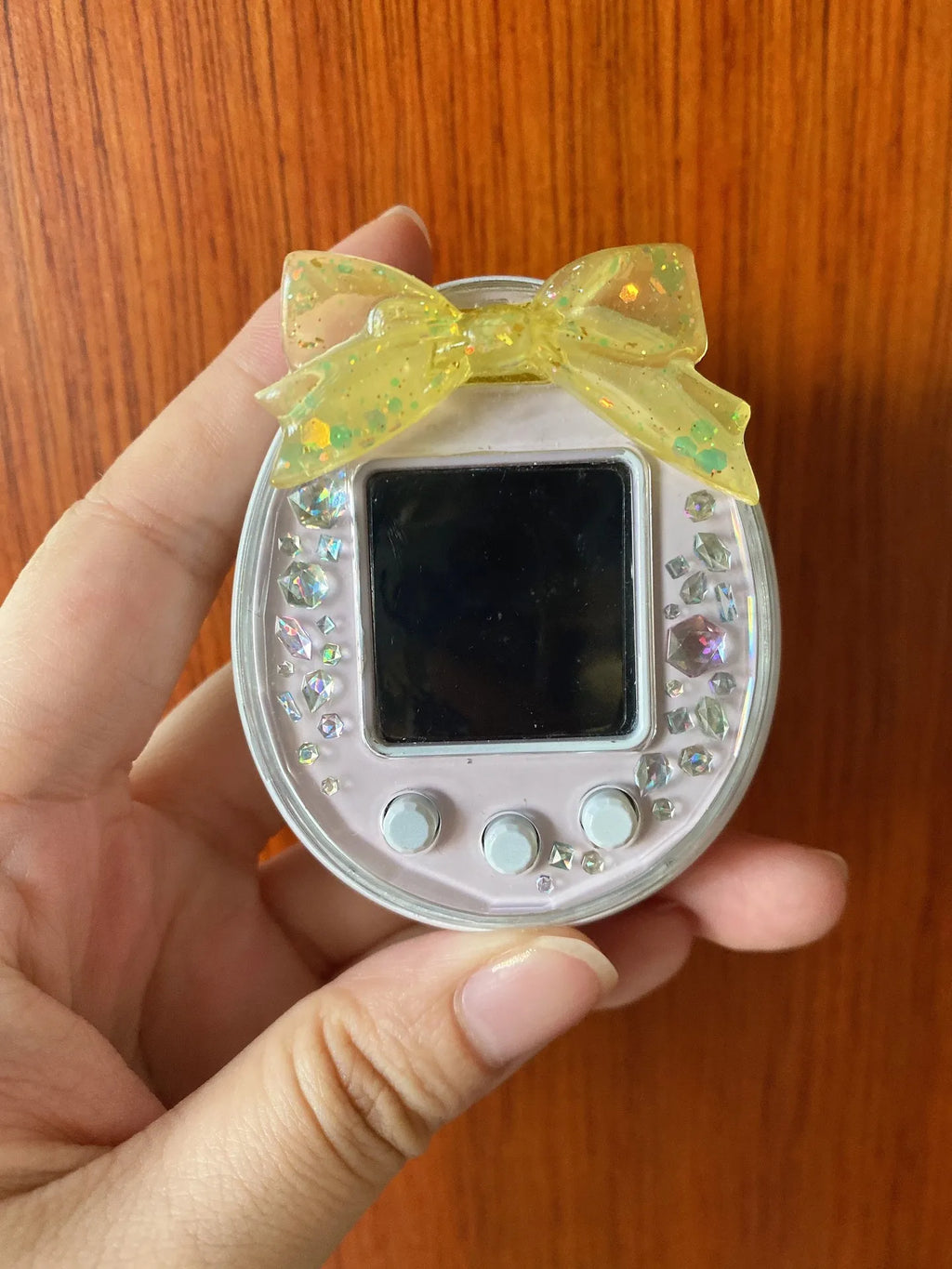 Tamagotchi Uni electronic pet with yellow resin bow and crystal dust plug for screen protection and stylish decor.