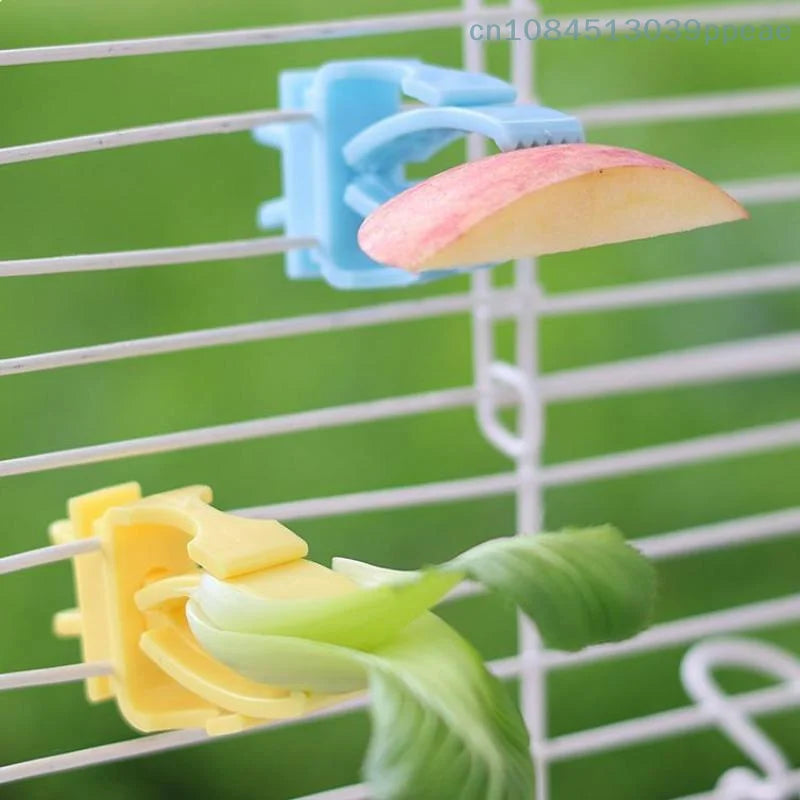 Blue and yellow plastic bird food clips holding fruit and vegetables on a bird cage for easy feeding.