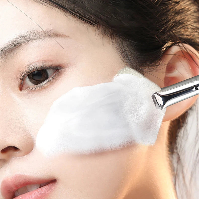 Soft facial mask brush applying white cleansing foam to skin for a portable skincare beauty routine.