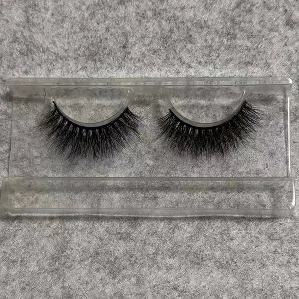 A pair of black 3D mink false eyelashes with a soft, wispy layered texture in a clear plastic tray.