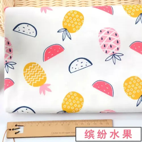 White knit jersey fabric with a colorful pineapple and watermelon fruit print, shown next to a 15cm wooden ruler.