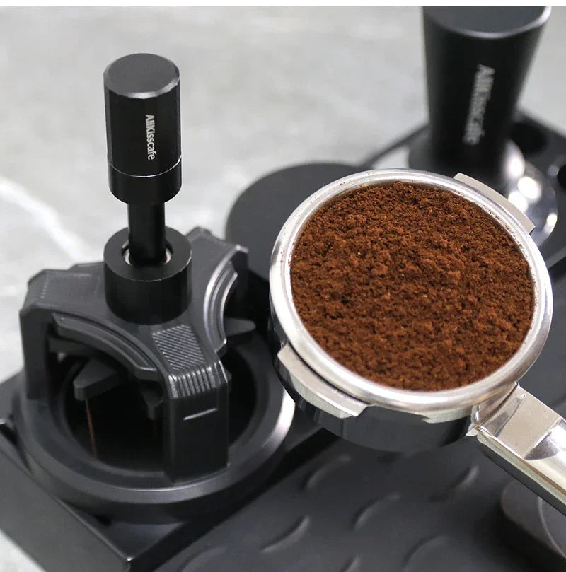 Alliksscafe matte black espresso coffee distributor and portafilter with ground coffee on a tamping station.
