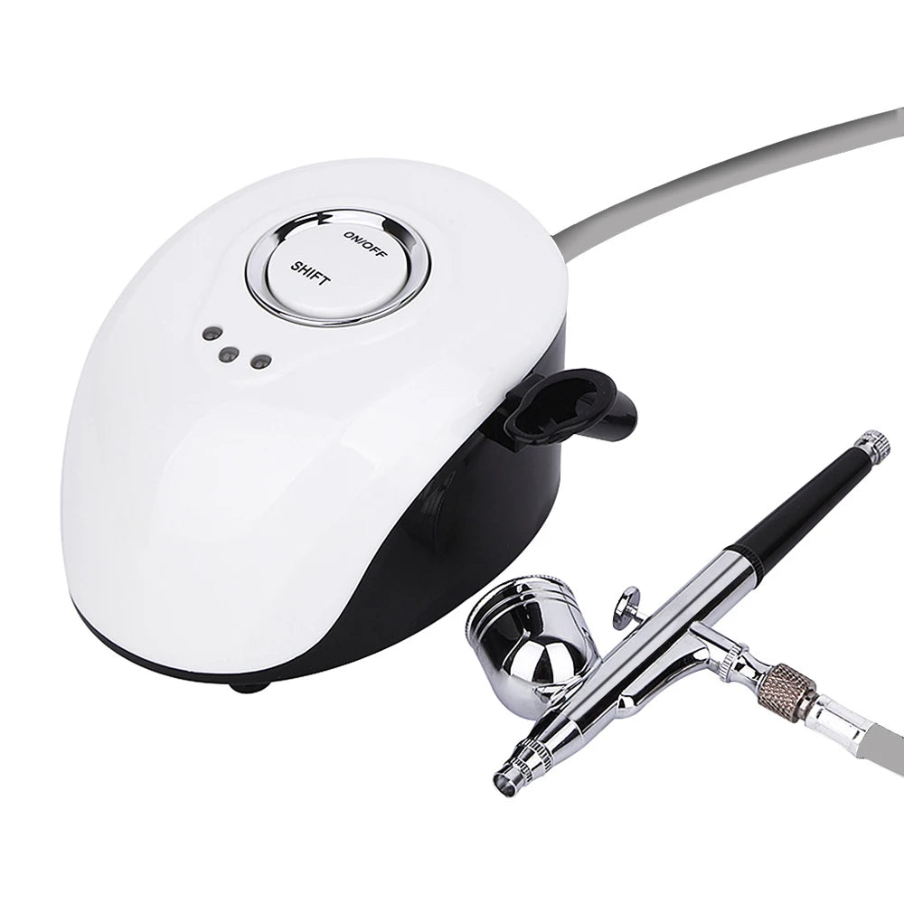White and black portable airbrush compressor with a chrome metal airbrush gun, connected by a flexible hose.