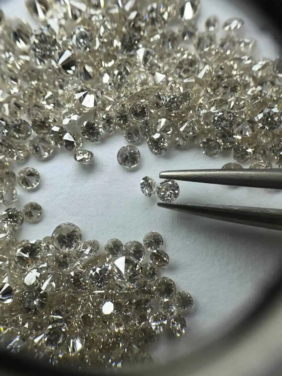 Loose round brilliant diamonds, white, close-up with metal tweezers holding one