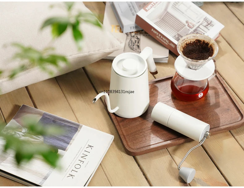 Matte white gooseneck kettle and manual coffee grinder set on a wooden tray with a glass pour-over dripper.