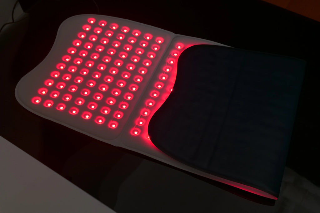 Large white rectangular red light therapy mat with a grid of glowing red LED lights, partially folded.