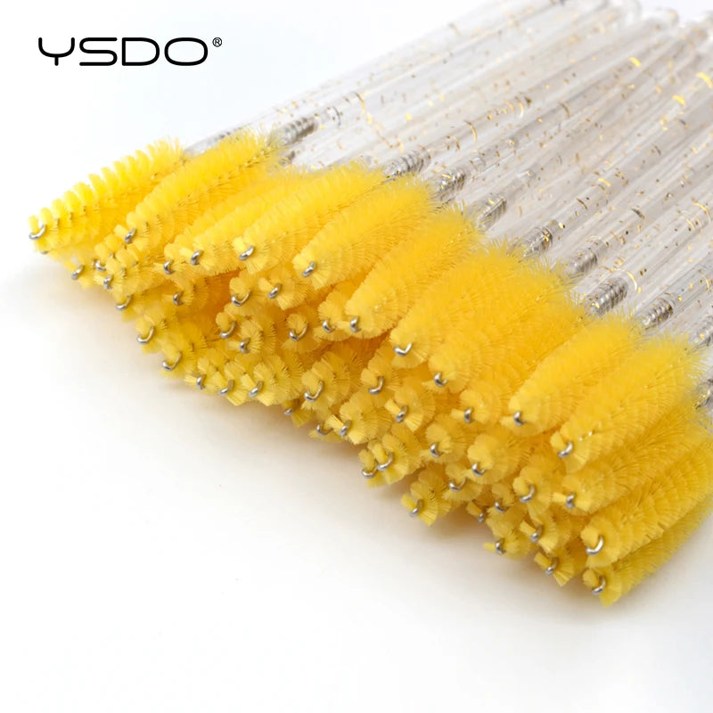 Disposable eyelash brushes with bright yellow nylon bristles and clear glittery plastic handles.