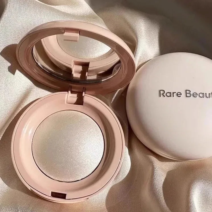 Rare Beauty highlighter powder compact in sleek pink case with mirror, featuring shimmery glow finish on satin fabric.