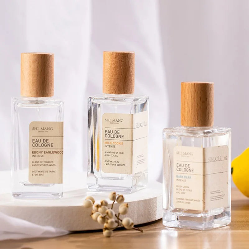 Three rectangular glass Eau de Cologne perfume bottles with cylindrical wooden caps on a white circular display stand.